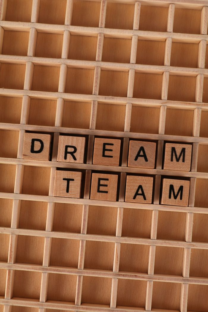 Wooden blocks spelling 'Dream Team' arranged on a wooden grid background.